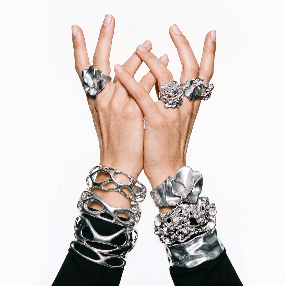 Dos manos alzadas juntas, con anillos de acero plegados, agrupados y reticulados, y brazaletes apilados