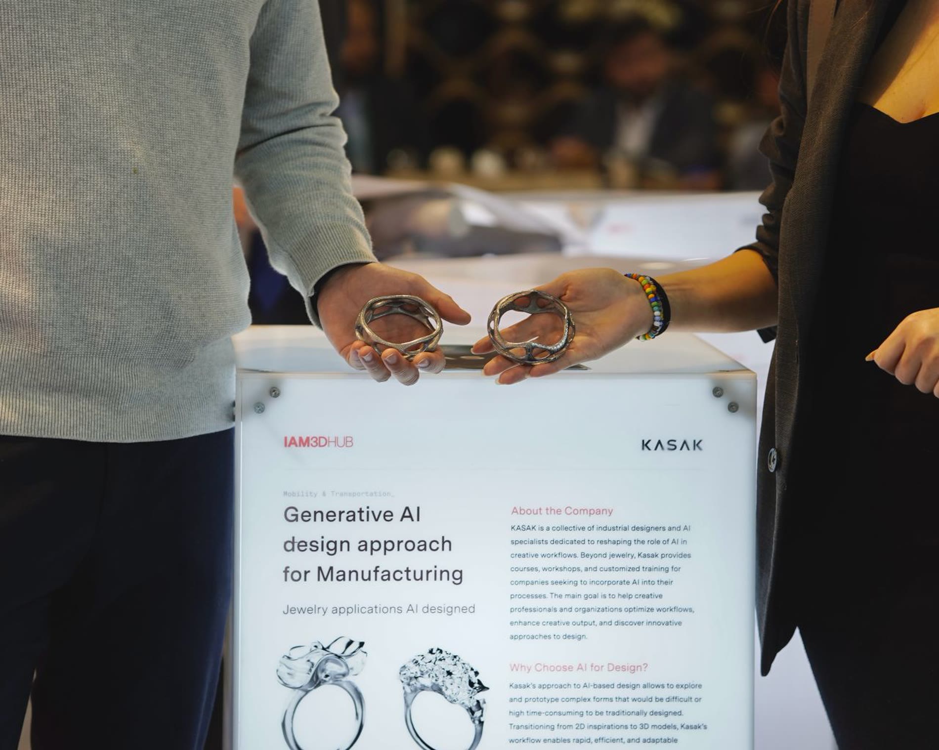 Two people holding printed steel rings above a stand at Formnext, beside a panel reading Generative AI design approach for Manufacturing