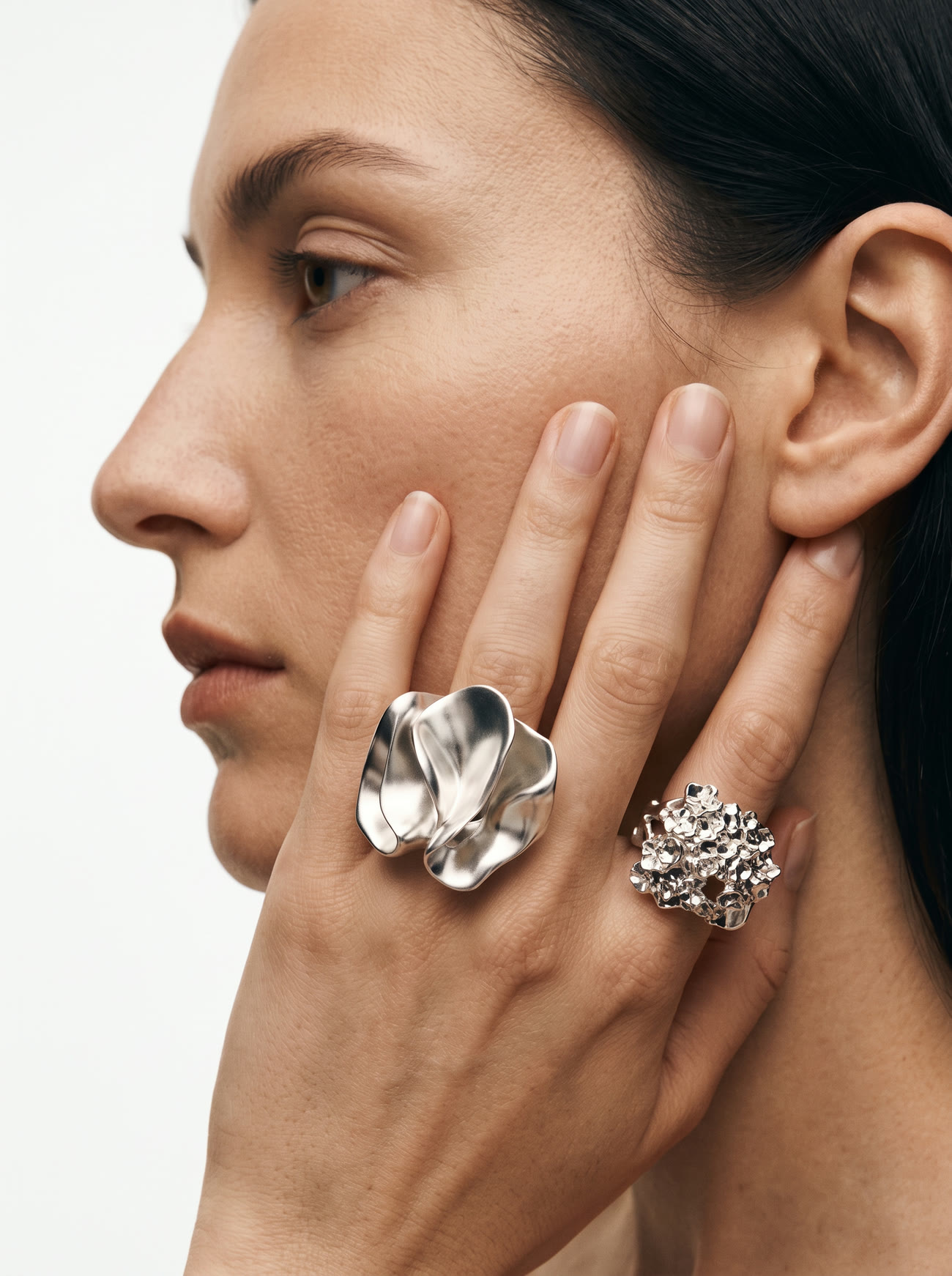 A woman in profile resting her hand against her face, wearing a folded steel ring and a mineral cluster ring