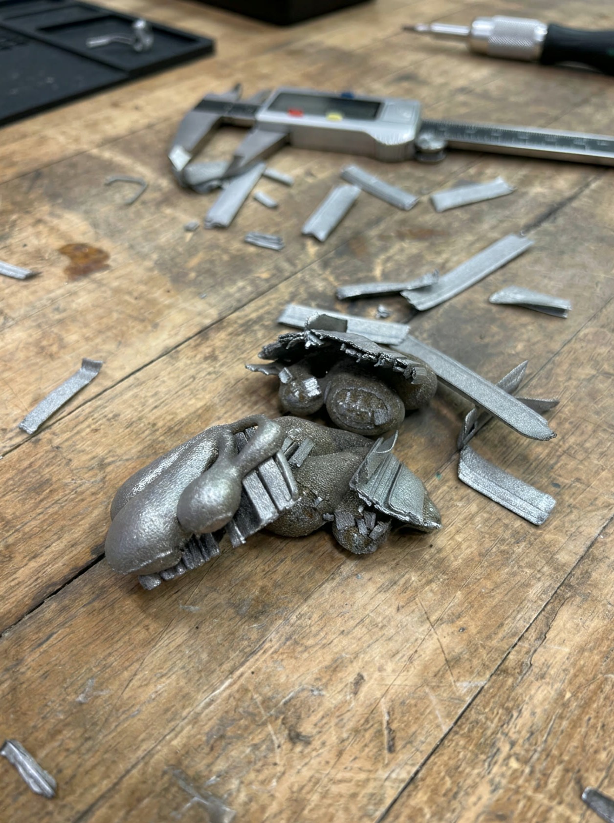 Cluster pieces as printed in grey steel on a workbench, supports cut away and scattered around them beside a caliper