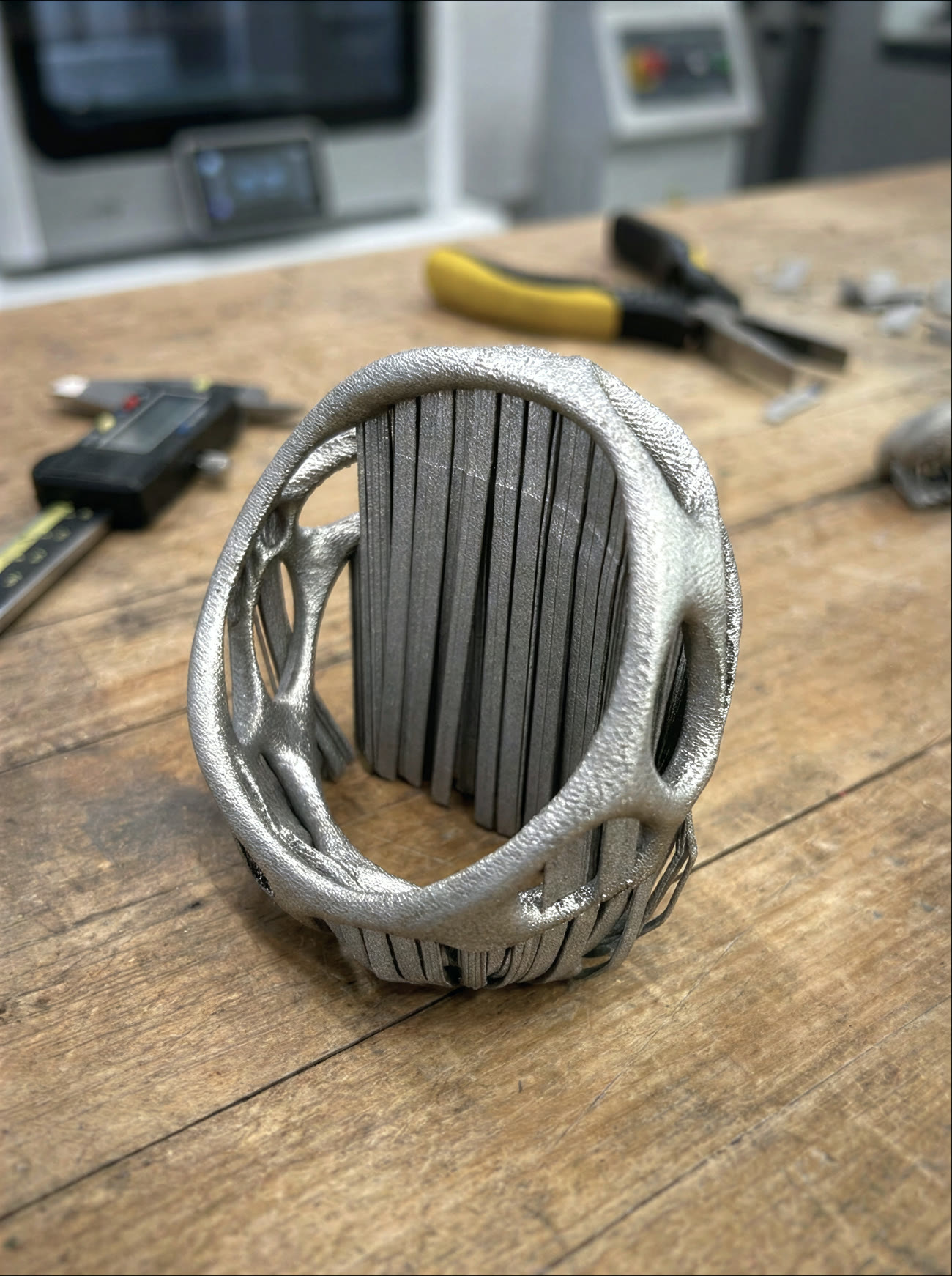 A latticed cuff as printed in matte grey steel, its interior still filled with a dense wall of support pillars