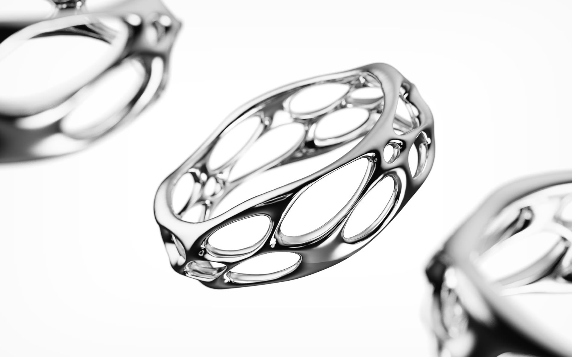 Close render of the latticed ring, its polished openings stretched around the band, with two more rings out of focus behind