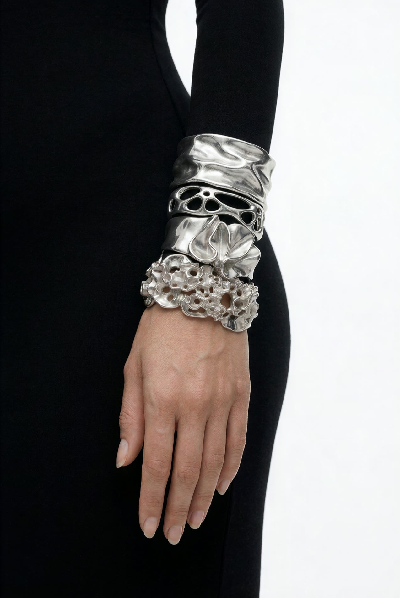 A wrist in a black sleeve wearing three stacked steel cuffs: a folded band, an open lattice and a mineral cluster