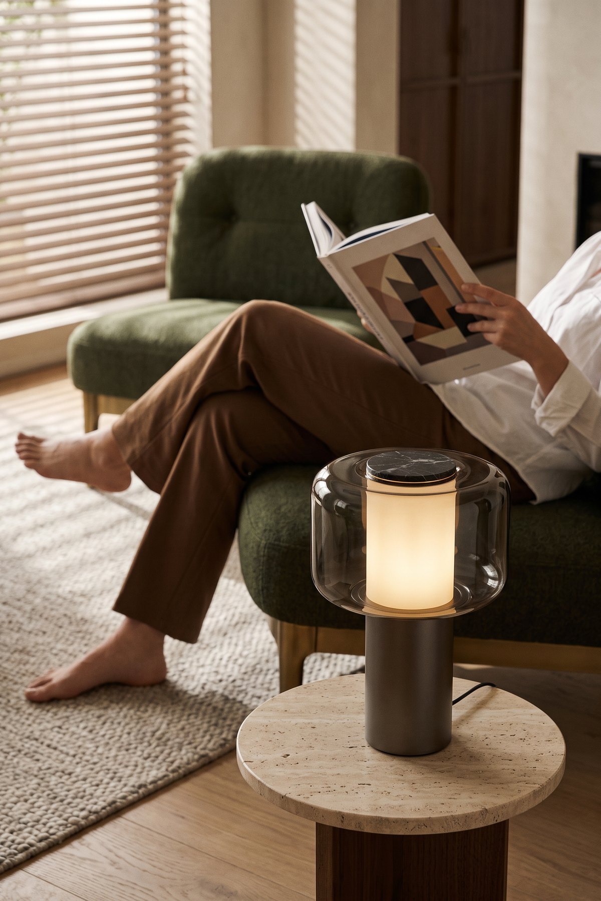 Someone reading in a green armchair, Lumen glowing on a travertine side table beside them